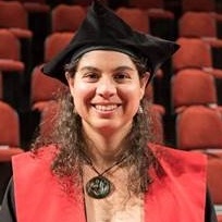 Picture of Cecile Massiot wearing graduation attire and smiling, with auditorium in background